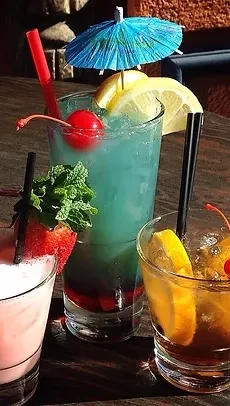 Three colorful garnished cocktails on a dark wooden table.