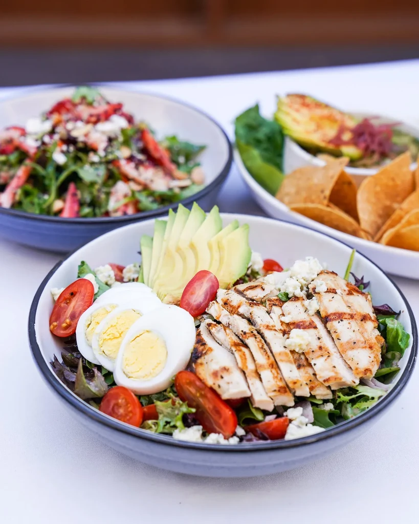 Grilled chicken salad, strawberry salad, guacamole, and tortilla chips.