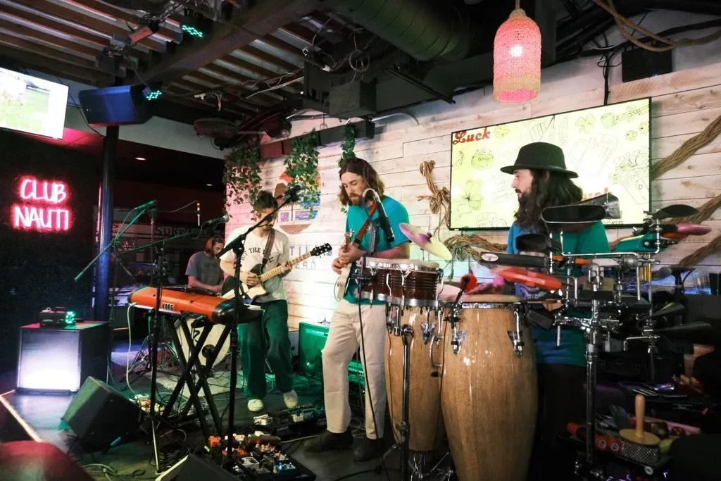 Four male musicians perform live on a dimly lit stage.