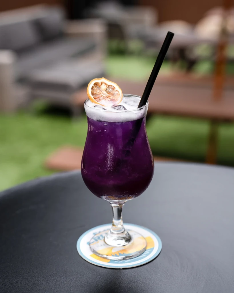 Purple stemmed drink with ice, froth, and orange garnish on patio.