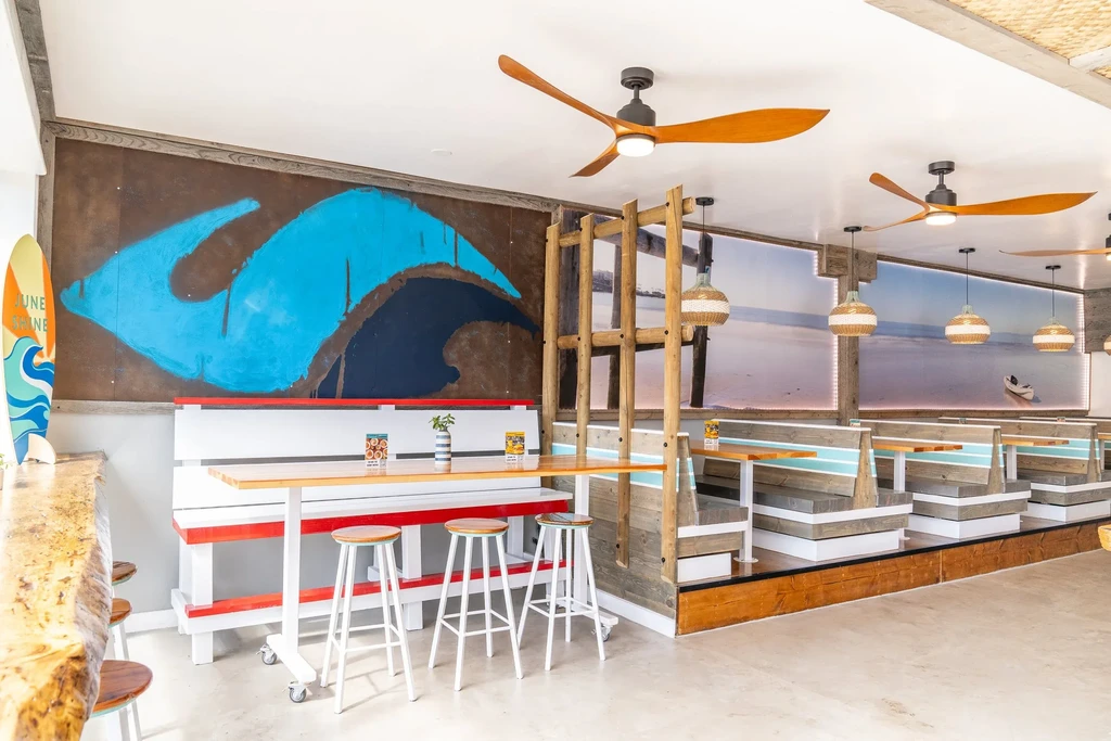 Bright, surf-themed restaurant interior with a bar, wave mural, and beach scene.