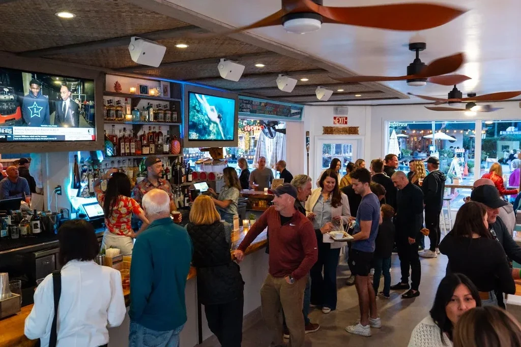 Lively bar and restaurant interior with people, TVs, and patio.