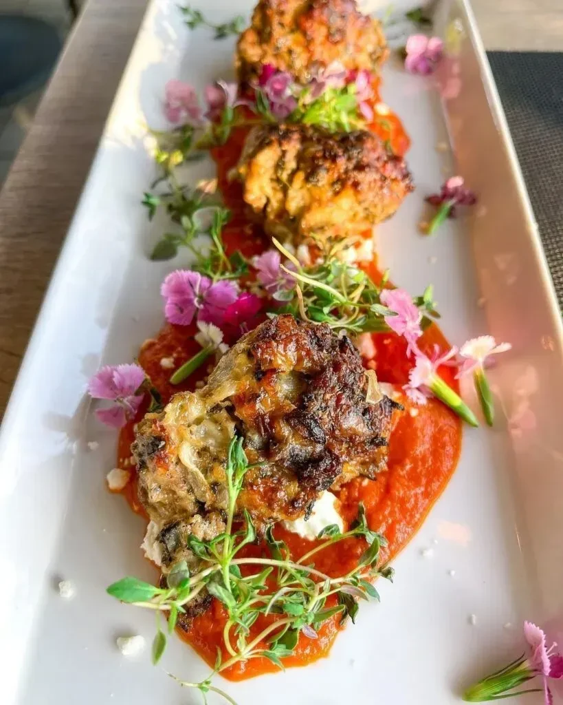 Three crispy fritters on tomato ragu with herbs and edible flowers.