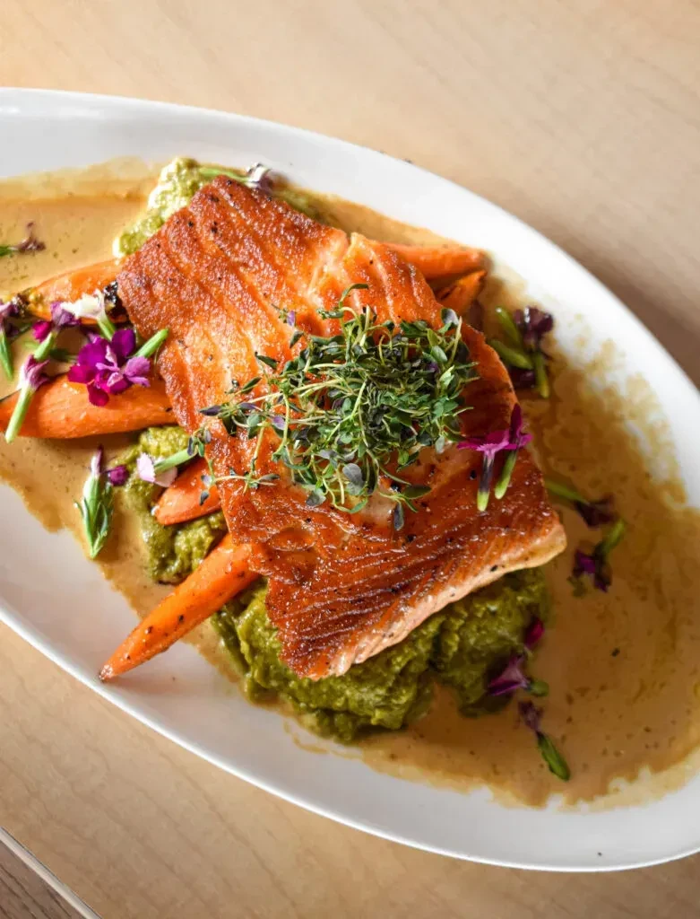 Grilled salmon with green puree, carrots, herbs, sauce, and flowers.