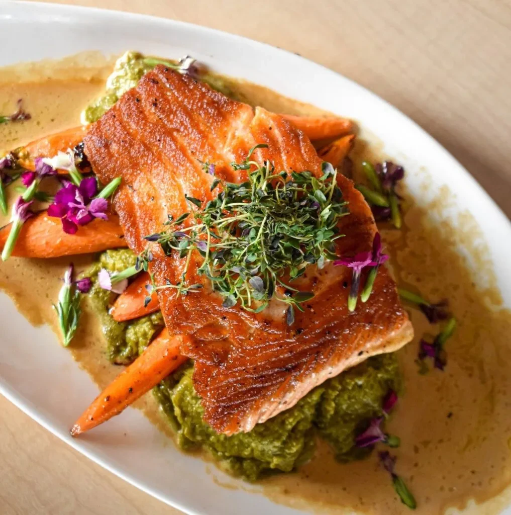 Pan-seared salmon with crispy skin, carrots, green purée, and edible flowers.