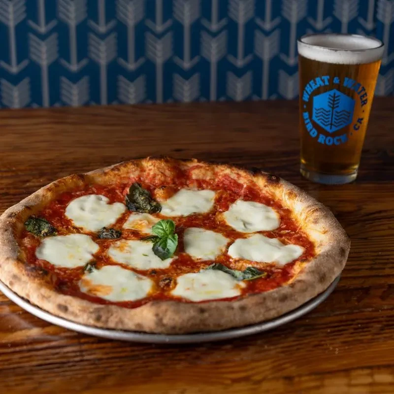 Margherita pizza, pint of beer, and blue patterned wall on a rustic table.