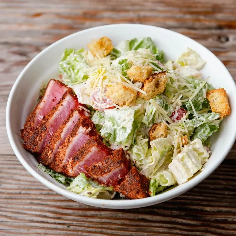 White bowl of Caesar salad with rare seared tuna slices.