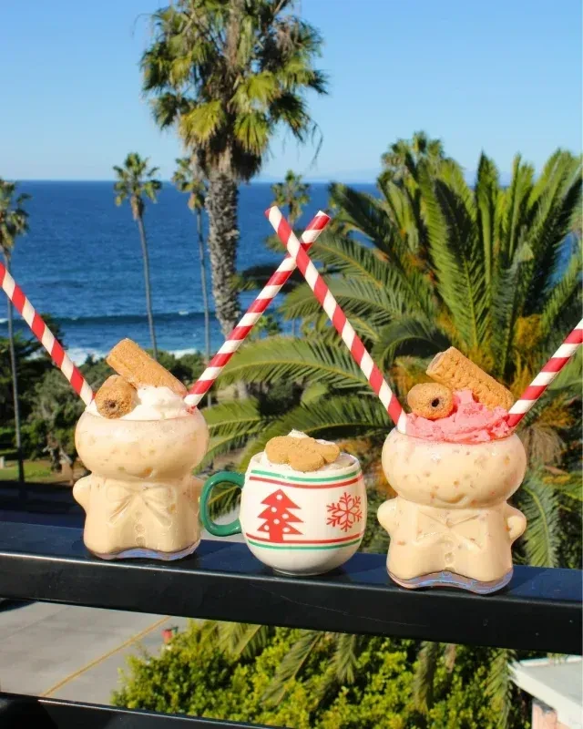 Festive gingerbread drinks on railing overlooking ocean and palm trees.