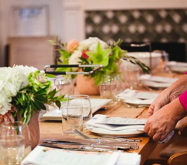Hands arranging menu on elegant wooden dining table with flowers.