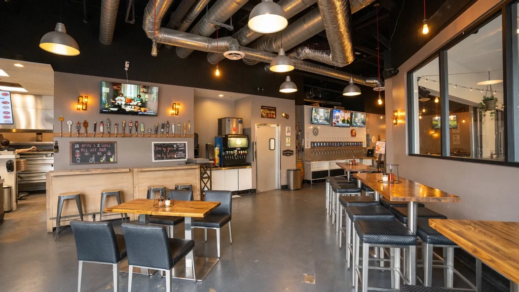 Modern industrial gastropub interior with varied seating, beer taps, and TVs.
