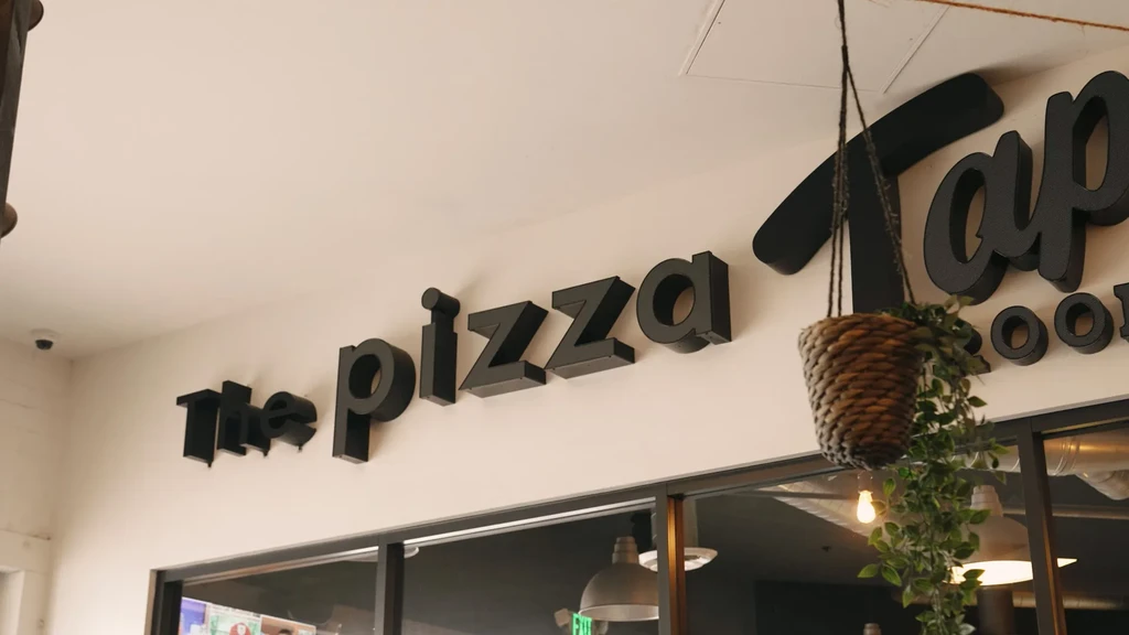 Modern restaurant interior with 'The Pizza' sign and hanging plant.