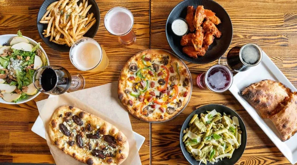 Overhead view: wooden table filled with diverse restaurant dishes and beverages.
