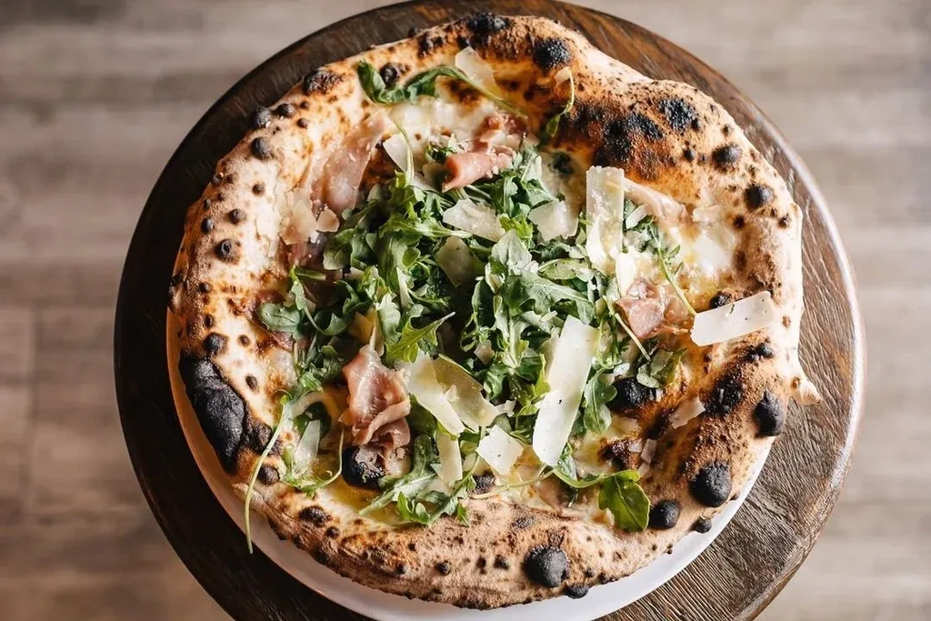 Overhead Neapolitan pizza with charred crust, arugula, prosciutto, and cheese.