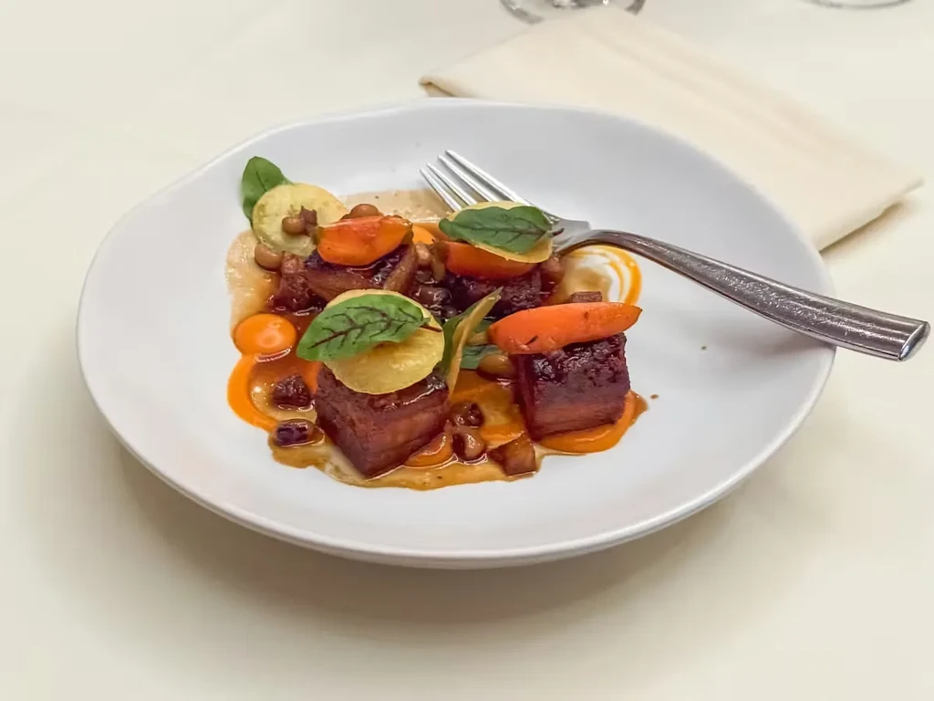 Elegantly plated gourmet meat, carrots, and chips with rich sauce.