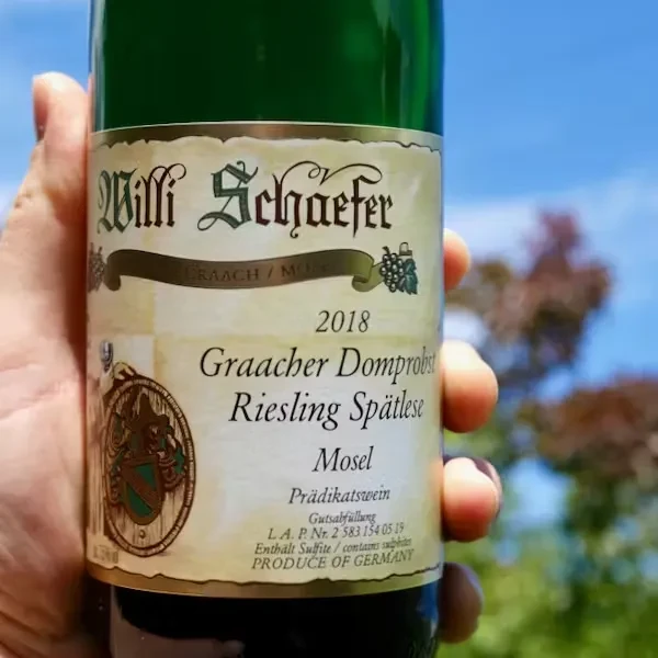 Willi Schaefer 2018 Mosel Riesling Spätlese bottle held against a sunny sky.