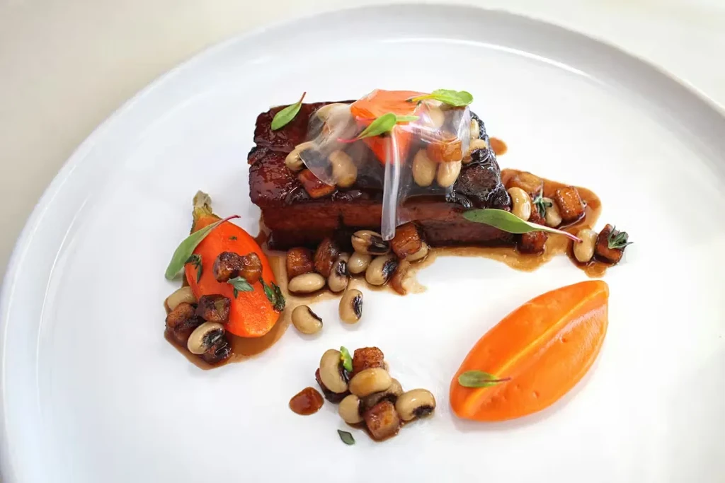 Artfully plated glazed meat, black-eyed peas, carrot, and orange puree.