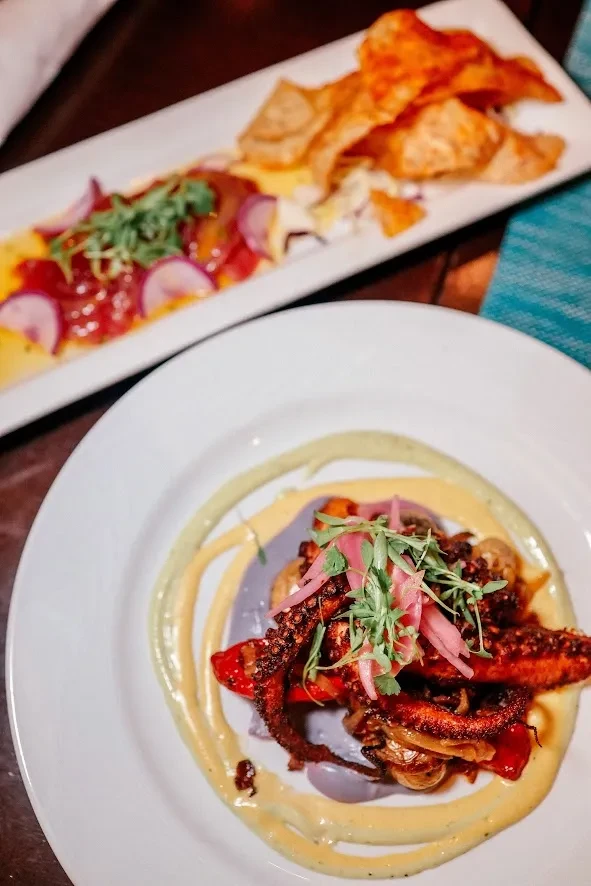 Grilled octopus with purple puree and sliced dish on dark table.