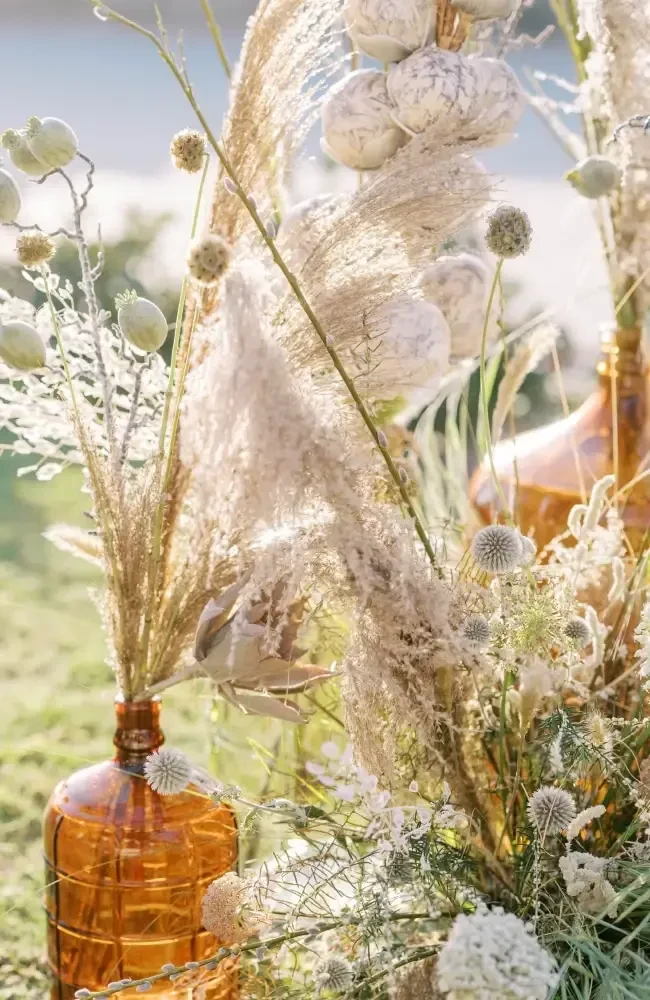 Dried pampas grass, thistle flowers, and seed pods in amber glass vases.