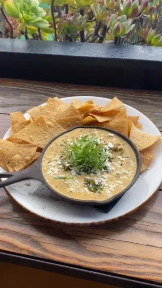 Skillet of cheesy green dip with crumbled cheese and tortilla chips.