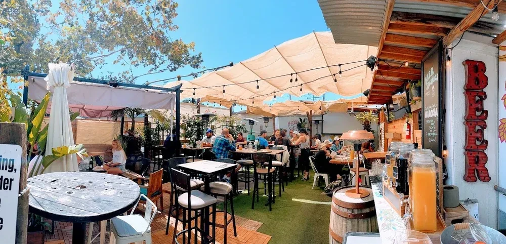 Vibrant outdoor beer garden with patrons, sun shades, and BEER sign.