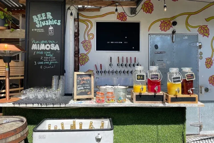 Outdoor self-serve mimosa bar with multiple juice dispensers and beer taps.