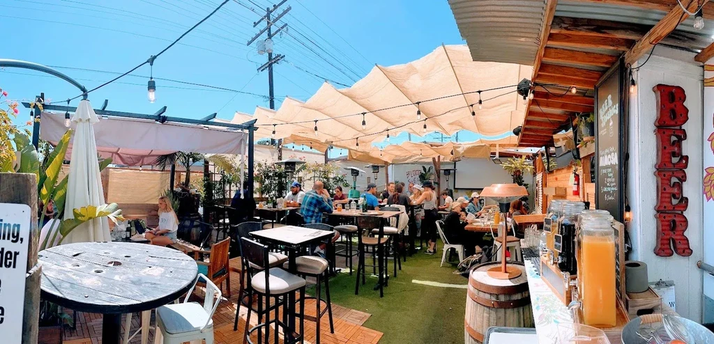 Busy sunny outdoor restaurant patio with shaded seating.
