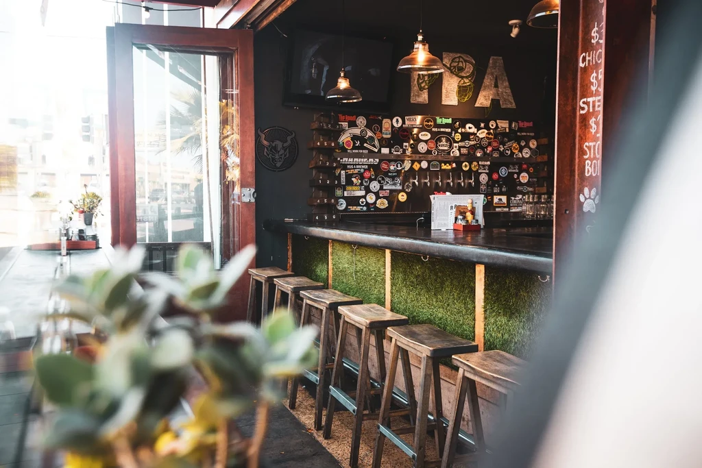 Bar counter with green grass panels, rustic stools, and beer taps.