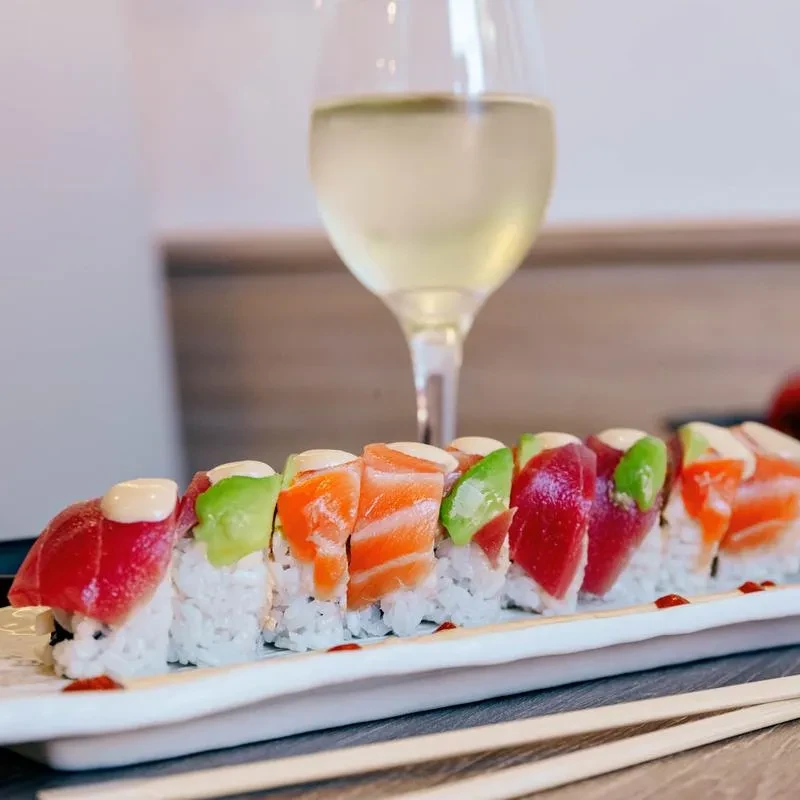 Close-up of sushi rolls with tuna, salmon, avocado, white wine, chopsticks.