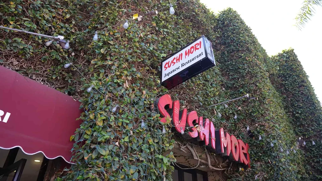 Sushi Mori restaurant exterior, ivy-covered, with signs and string lights.