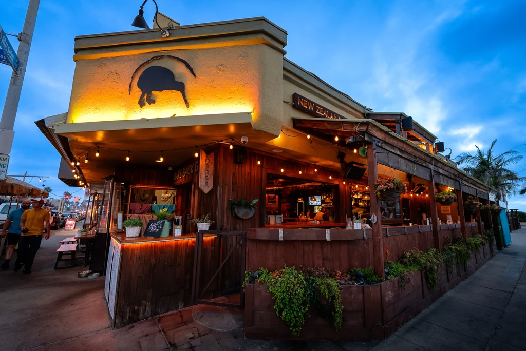 Rustic New Zealand bar exterior with kiwi bird logo and string lights.