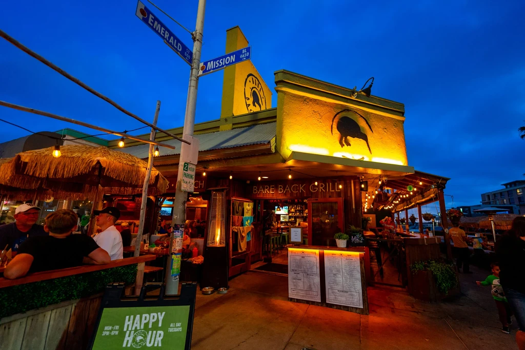 Bare Back Grill's lively yellow exterior at dusk with illuminated Kiwi logo.