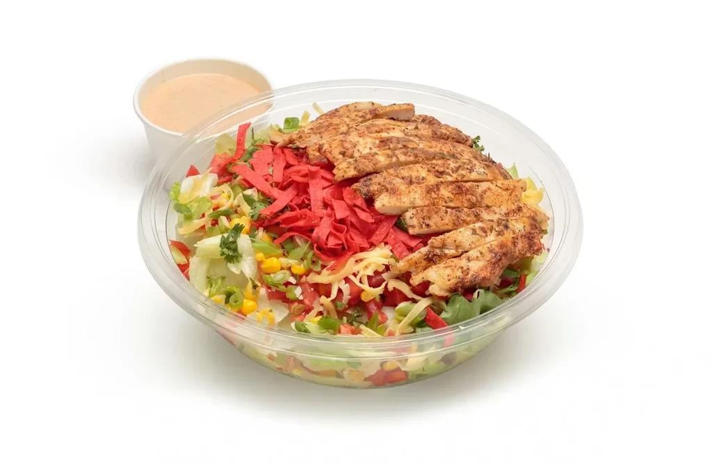 Grilled chicken salad in a clear to-go container with creamy dressing.