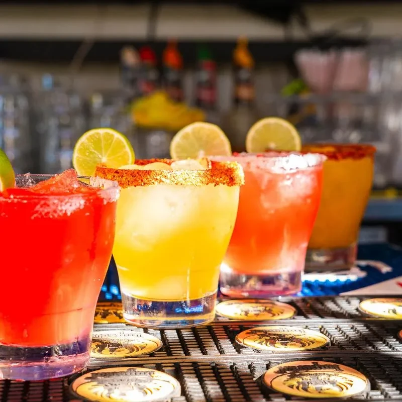 Four vibrant cocktails with citrus garnishes on a bar.