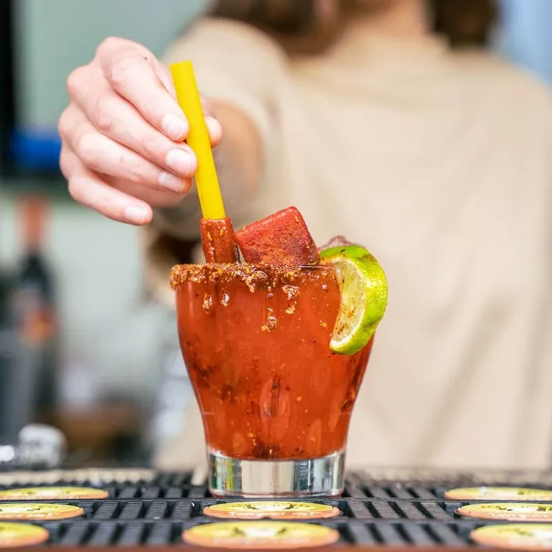 Thick red drink with seasoned rim, lime, chili fruit, and straw.