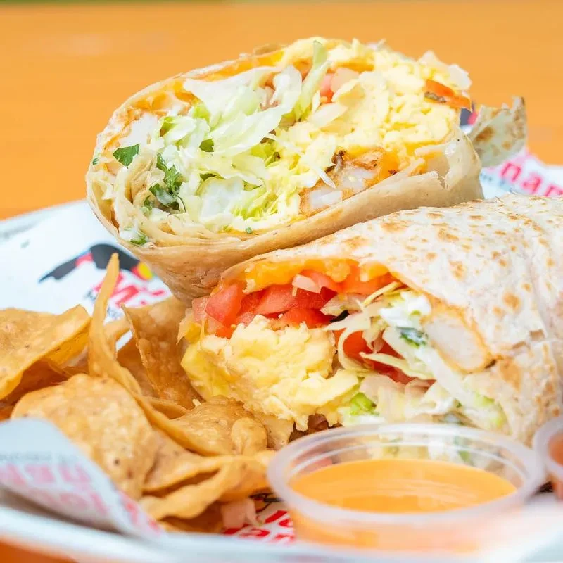 Cut burrito showing eggs, meat, lettuce, chips, and orange sauce.