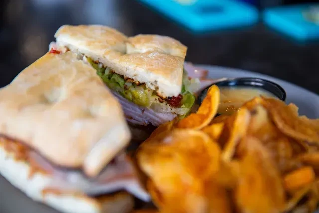 Rustic sandwich, hand-cut chips, and dipping sauce on a plate.