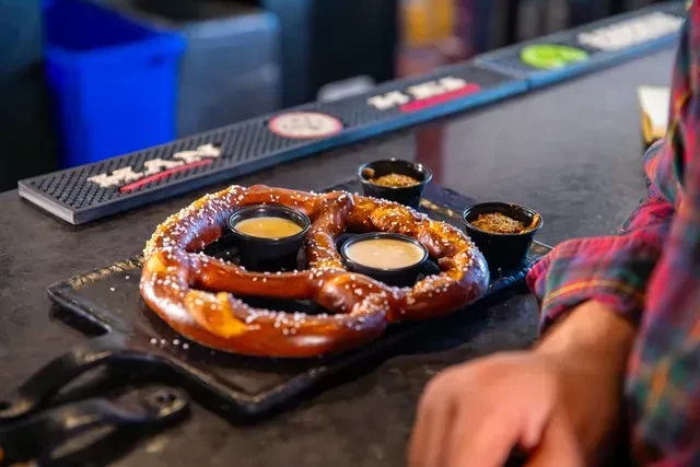 Large soft pretzel with salt and dipping sauces on a dark board.