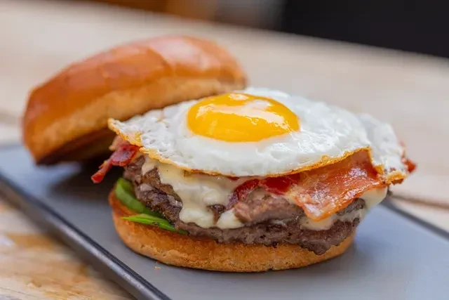 Open-faced burger showing patty, melted cheese, bacon, egg, and lettuce.