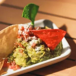 Guacamole topped with tomatoes, cheese, and colorful tortilla chips in a dish.