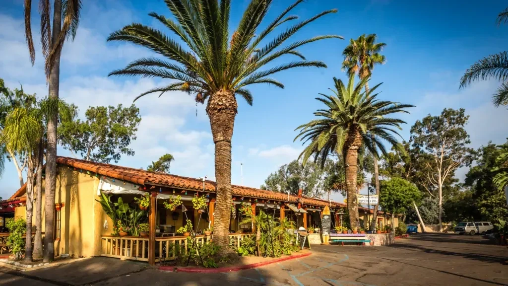 Yellow stucco building with terracotta roof, patio, and palm trees.