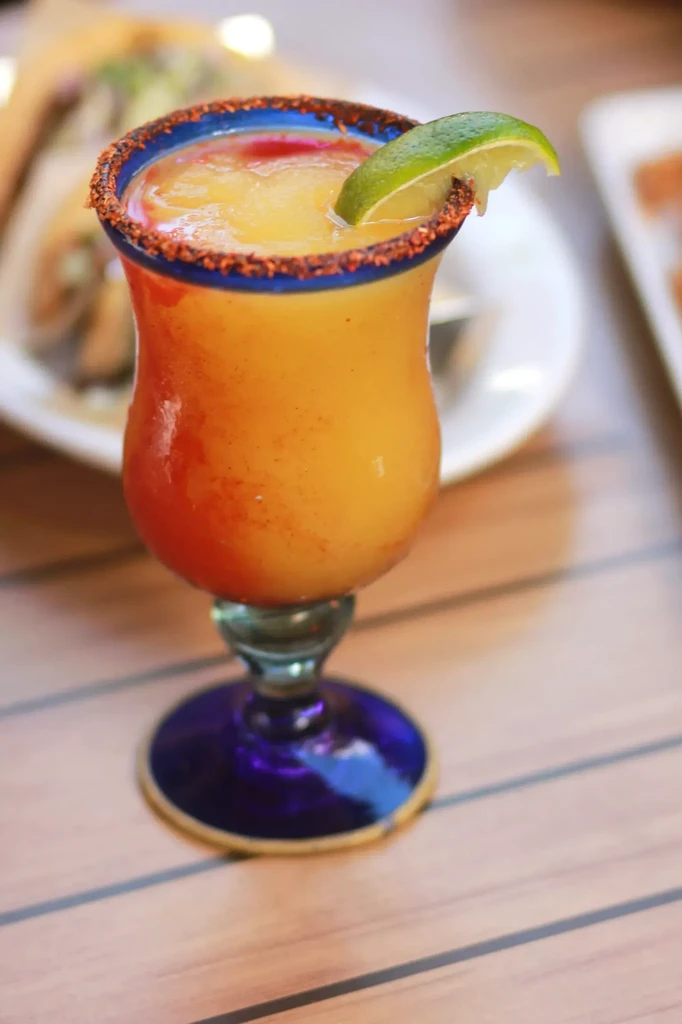 Vibrant ombre frozen cocktail with spiced rim, lime, and blue glass.