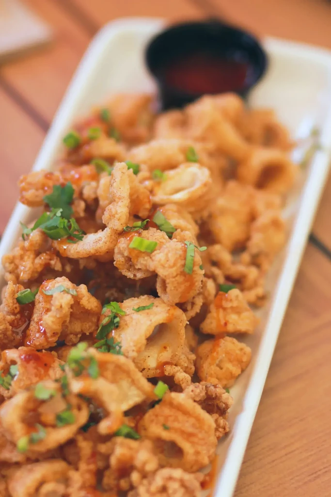 Golden-brown fried calamari garnished with herbs and red sauce on wood.
