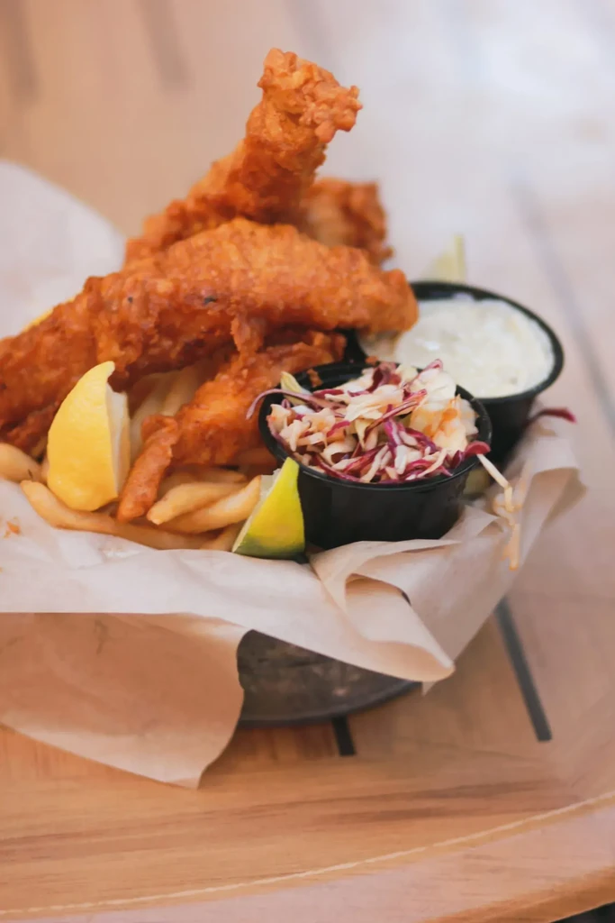 Fish and chips in a basket with coleslaw, tartar, lemon, lime.