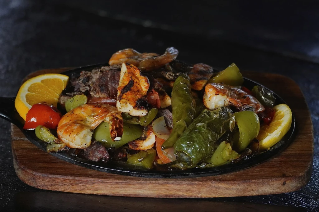 Sizzling shrimp, chicken, beef fajitas with peppers and onions in a skillet.