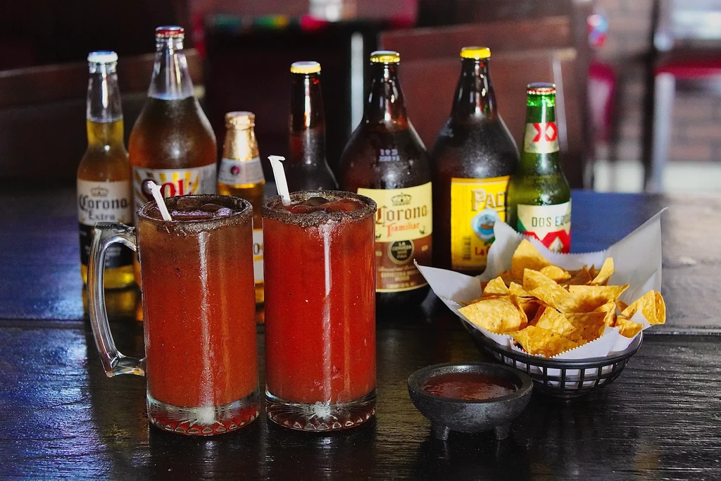 Table with two micheladas, tortilla chips, salsa, and Mexican beers.