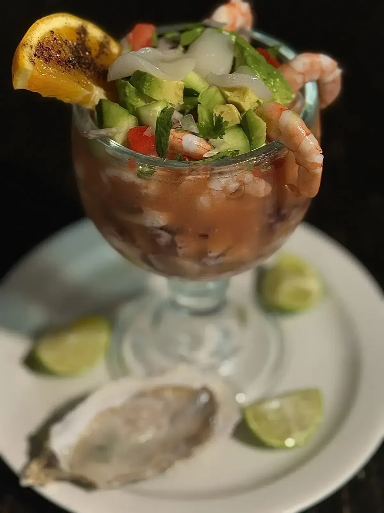 Shrimp cocktail in glass with avocado, tomato, orange, and oyster.