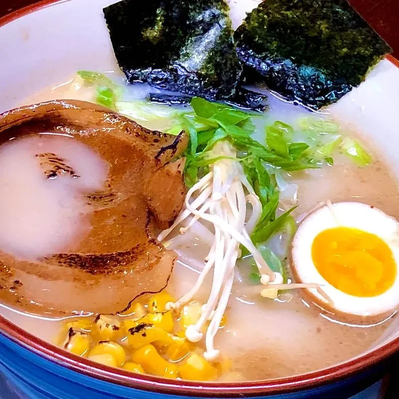 Close-up of a vibrant ramen bowl with pork, egg, corn, and nori.