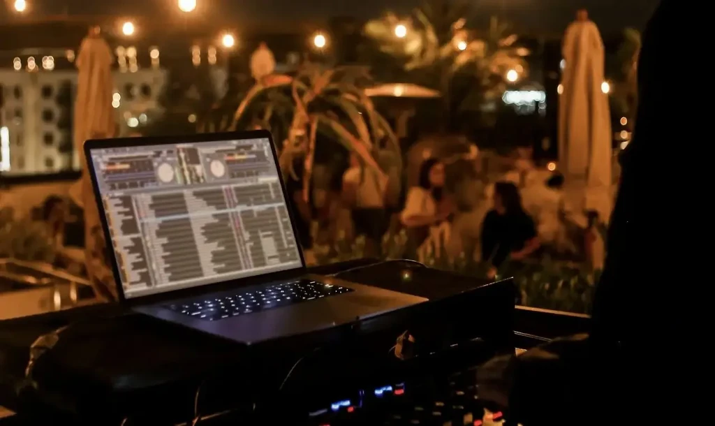 Laptop displaying DJ software at a string-lit outdoor bar.