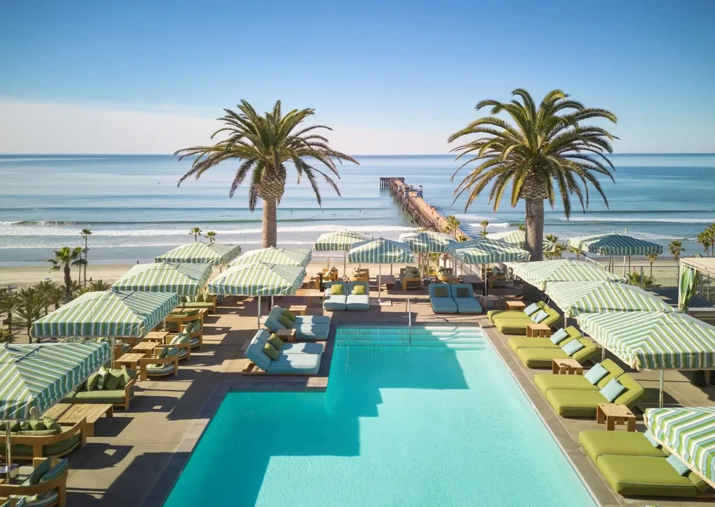 Aerial view of resort pool, beach, ocean, pier, and palm trees.
