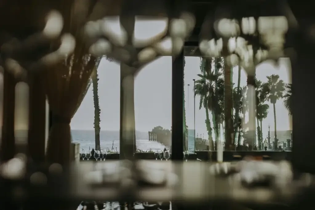 Blurry interior foreground with sharp ocean view of pier and palms.